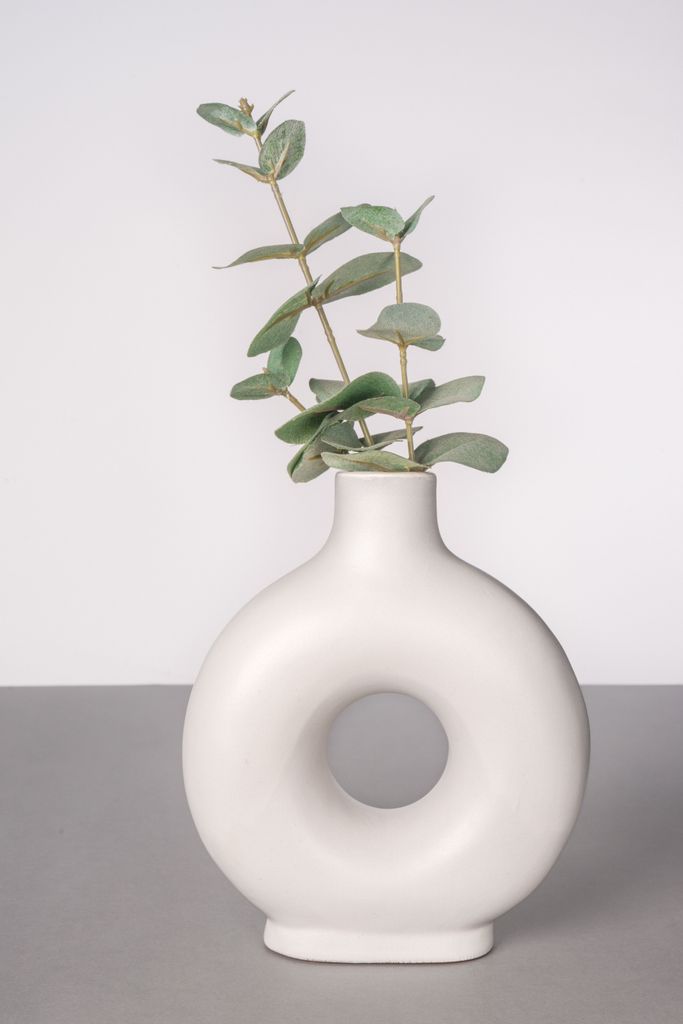 A modern white circular ceramic vase holding green eucalyptus branches.
