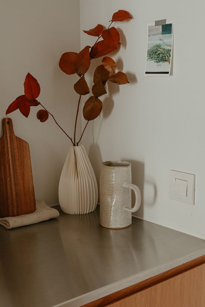 A serene kitchen shelf showcasing a minimalist setup with a modern vase and red leaves.