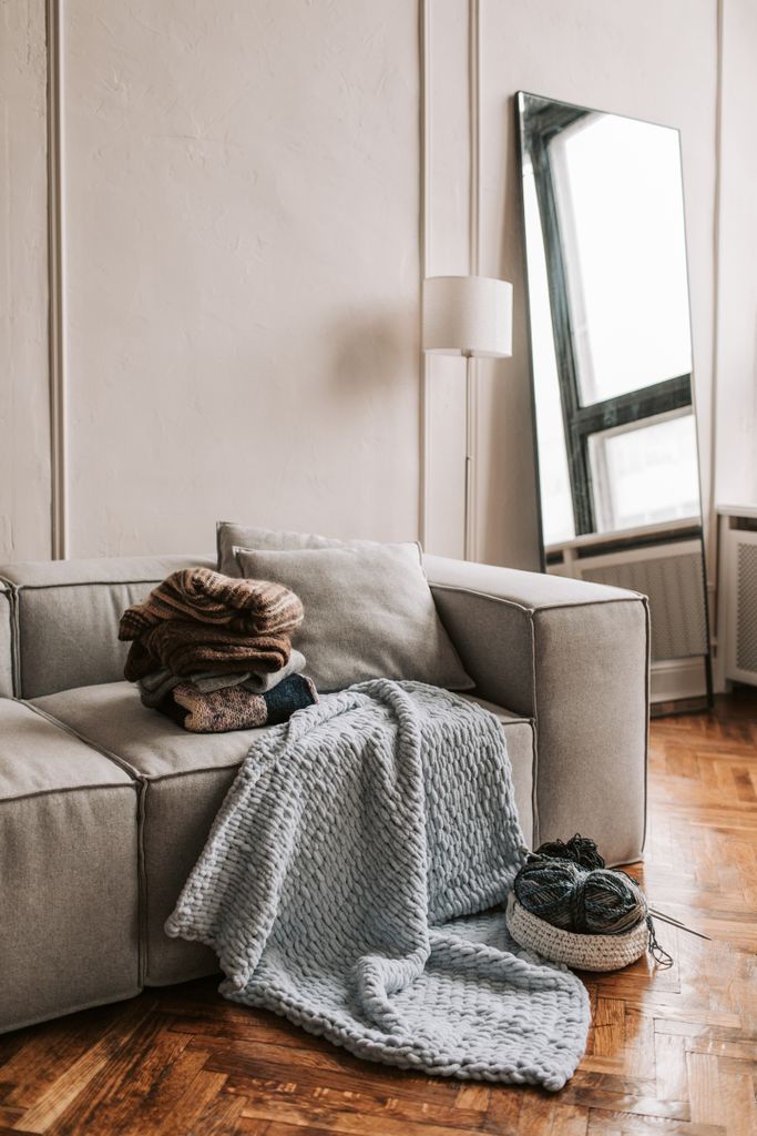 A modern living room featuring a sofa with knitted blankets and a floor mirror.
